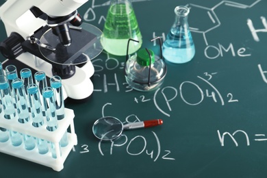 Laboratory glassware and microscope on blackboard with chemical formulas