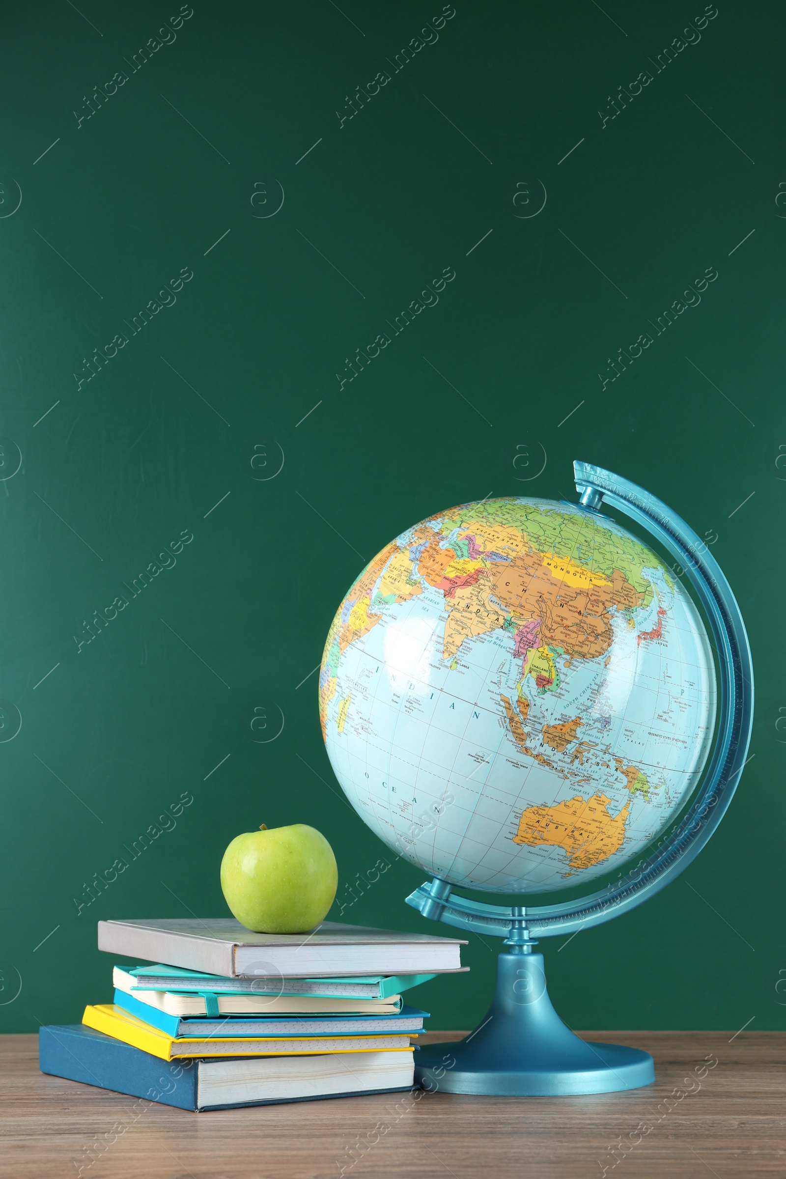 Photo of Globe, books and apple on wooden table near green chalkboard. Geography lesson