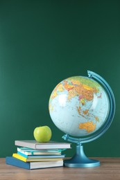Globe, books and apple on wooden table near green chalkboard. Geography lesson