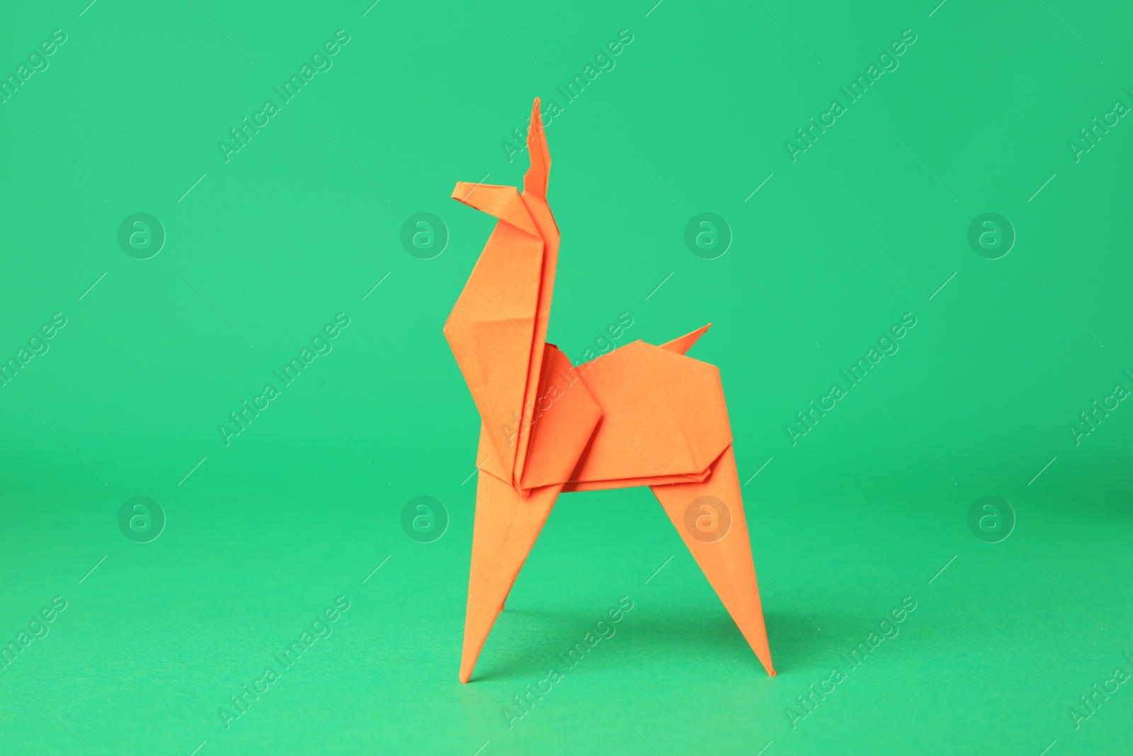 Photo of Origami art. Handmade orange paper deer on green background