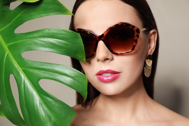 Photo of Beautiful woman in stylish sunglasses with tropical leaf on beige background