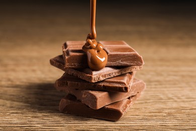 Photo of Pouring tasty milk chocolate paste onto pieces on wooden table, closeup