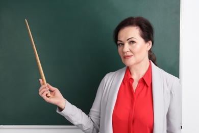 Photo of Portrait of female teacher with pointer near chalkboard in classroom