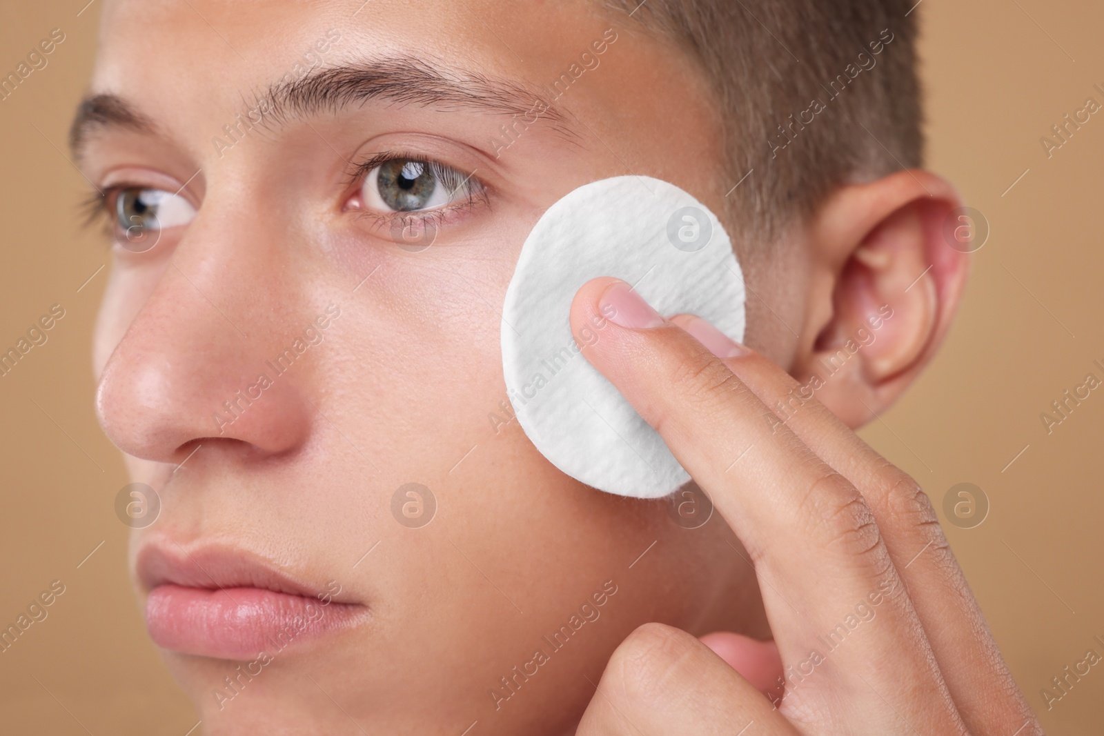 Photo of Handsome man cleaning face with cotton pad on beige background, closeup