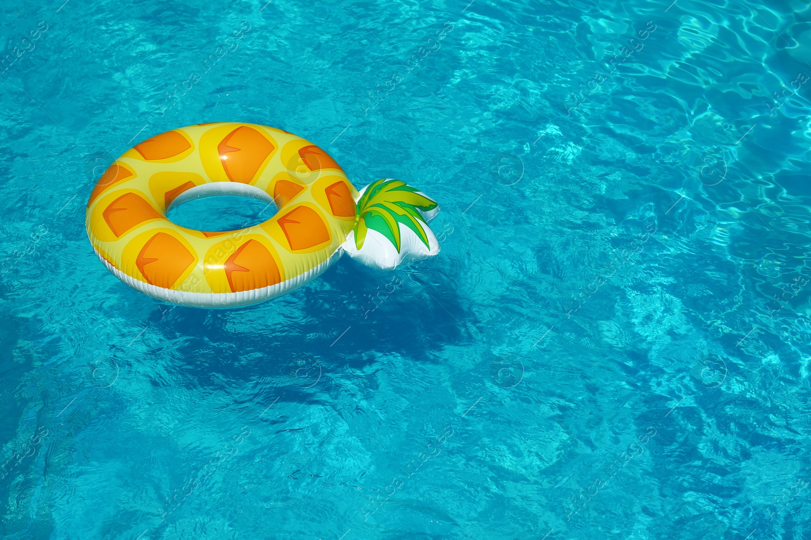 Photo of Bright inflatable pineapple ring floating in swimming pool on sunny day. Space for text