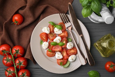 Tasty salad Caprese with mozarella balls, tomatoes and basil served on grey wooden table, flat lay
