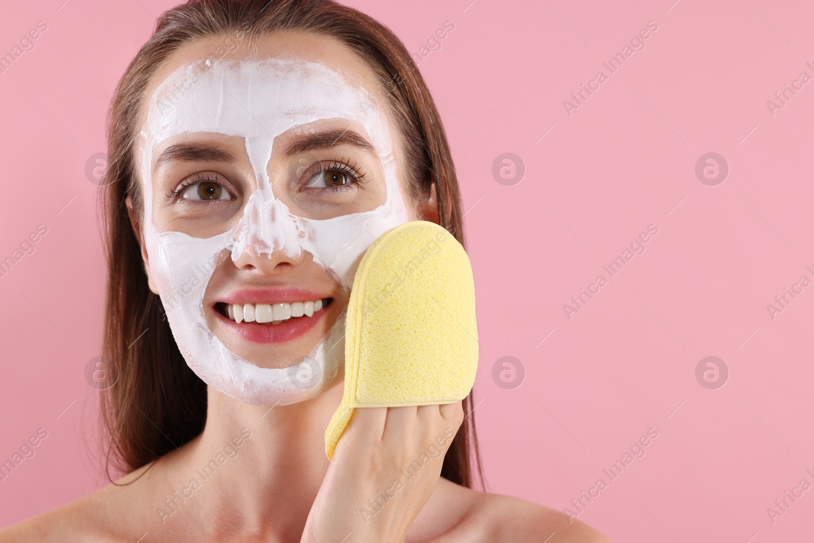 Photo of Happy young woman with face mask and sponge on pink background. Space for text