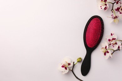 Photo of Stylish hairbrush and orchid flowers on white background, top view. Space for text
