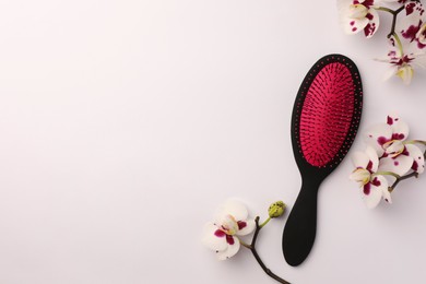 Stylish hairbrush and orchid flowers on white background, top view. Space for text