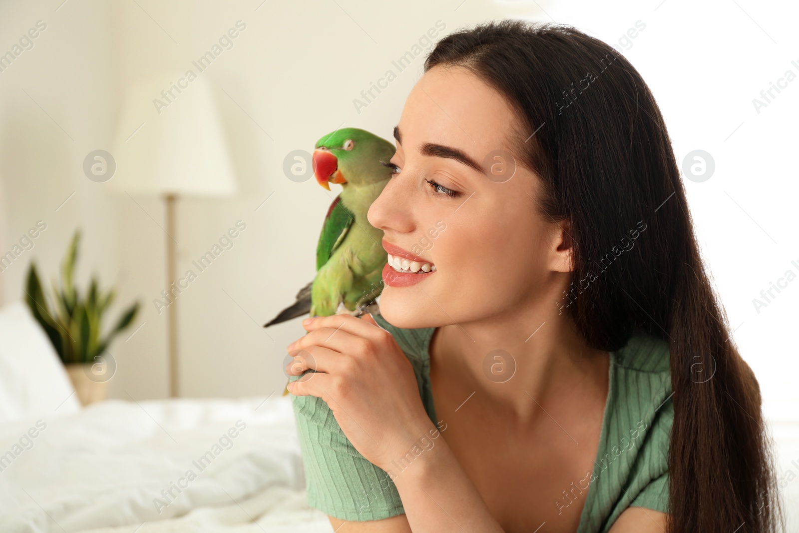 Photo of Young woman with Alexandrine parakeet indoors. Cute pet