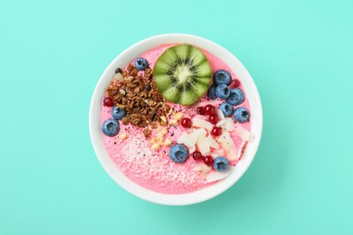 Photo of Tasty smoothie bowl with fresh kiwi fruit, berries and granola on turquoise background, top view
