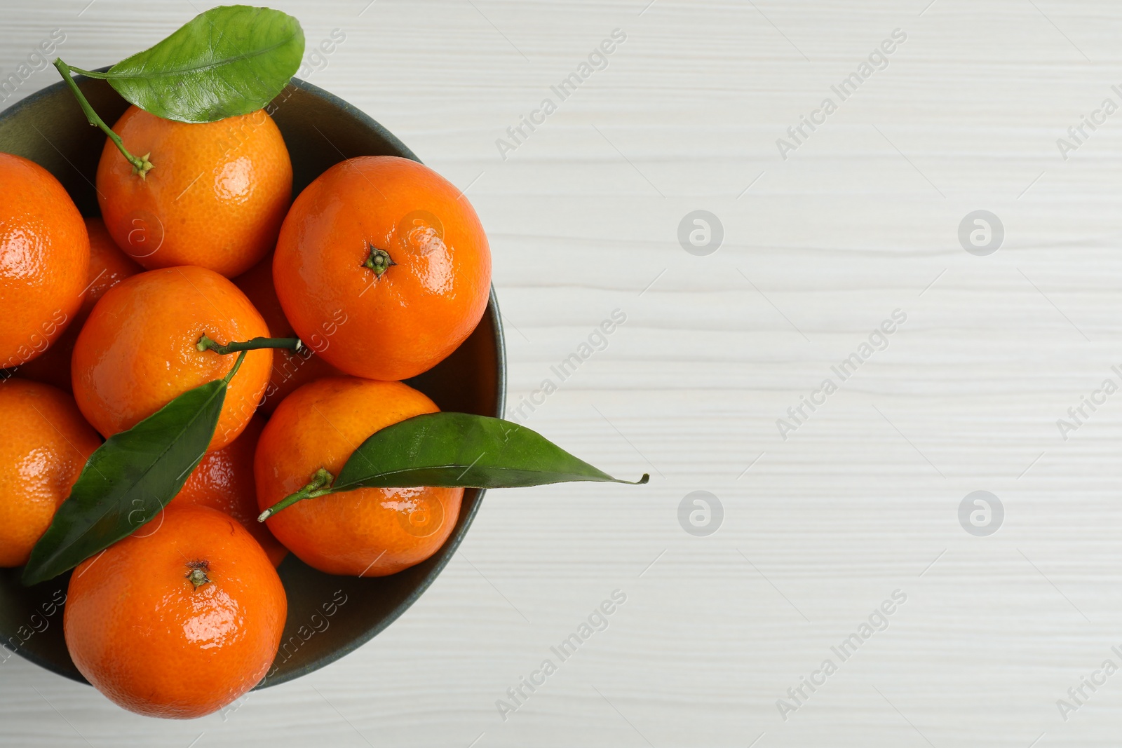 Photo of Delicious tangerines with green leaves in bowl on white wooden table, top view. Space for text