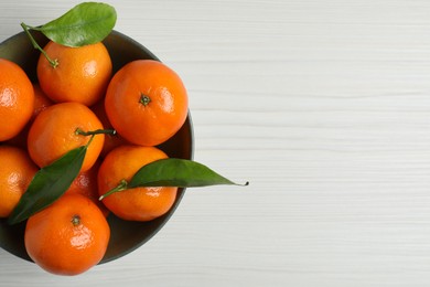 Delicious tangerines with green leaves in bowl on white wooden table, top view. Space for text