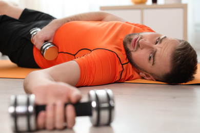 Photo of Lazy young man with sport equipment on yoga mat at home