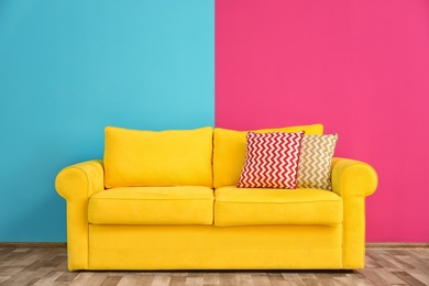 Photo of Sofa with different pillows near color wall in room