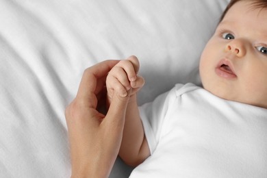 Mother holding hand of her little baby on bed, closeup