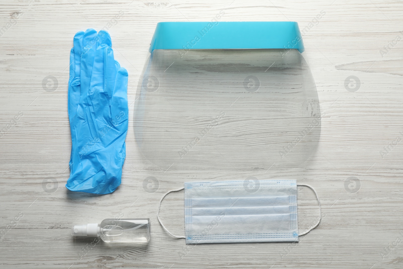 Photo of Medical gloves, mask, hand sanitizer and face shield on wooden background, flat lay. Safety equipment