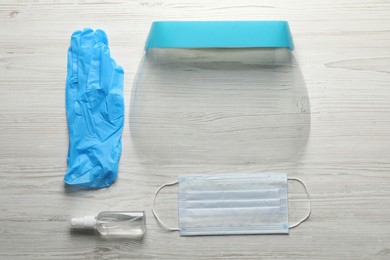 Medical gloves, mask, hand sanitizer and face shield on wooden background, flat lay. Safety equipment