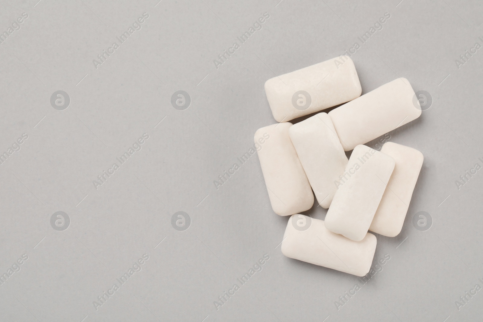 Photo of Many chewing gum pieces on light grey background, flat lay. Space for text