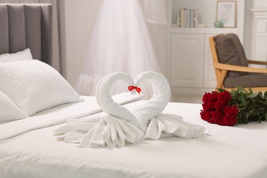 Photo of Honeymoon. Swans made of towels and beautiful red roses on bed in room