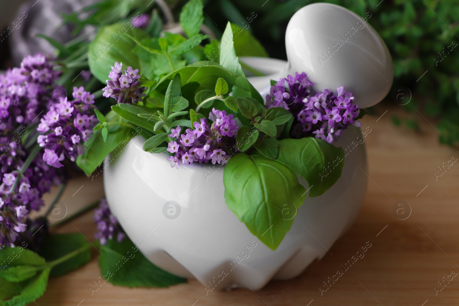 Photo of Mortar with fresh lavender flowers, herbs and pestle on wooden table, closeup