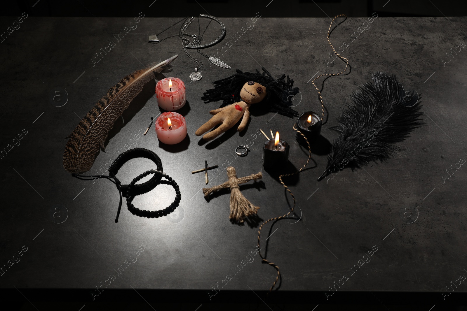 Photo of Female voodoo doll with pin in heart and ceremonial items on grey table