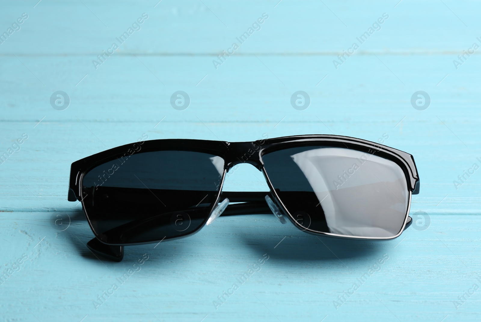 Photo of Stylish sunglasses on blue wooden background. Fashionable accessory