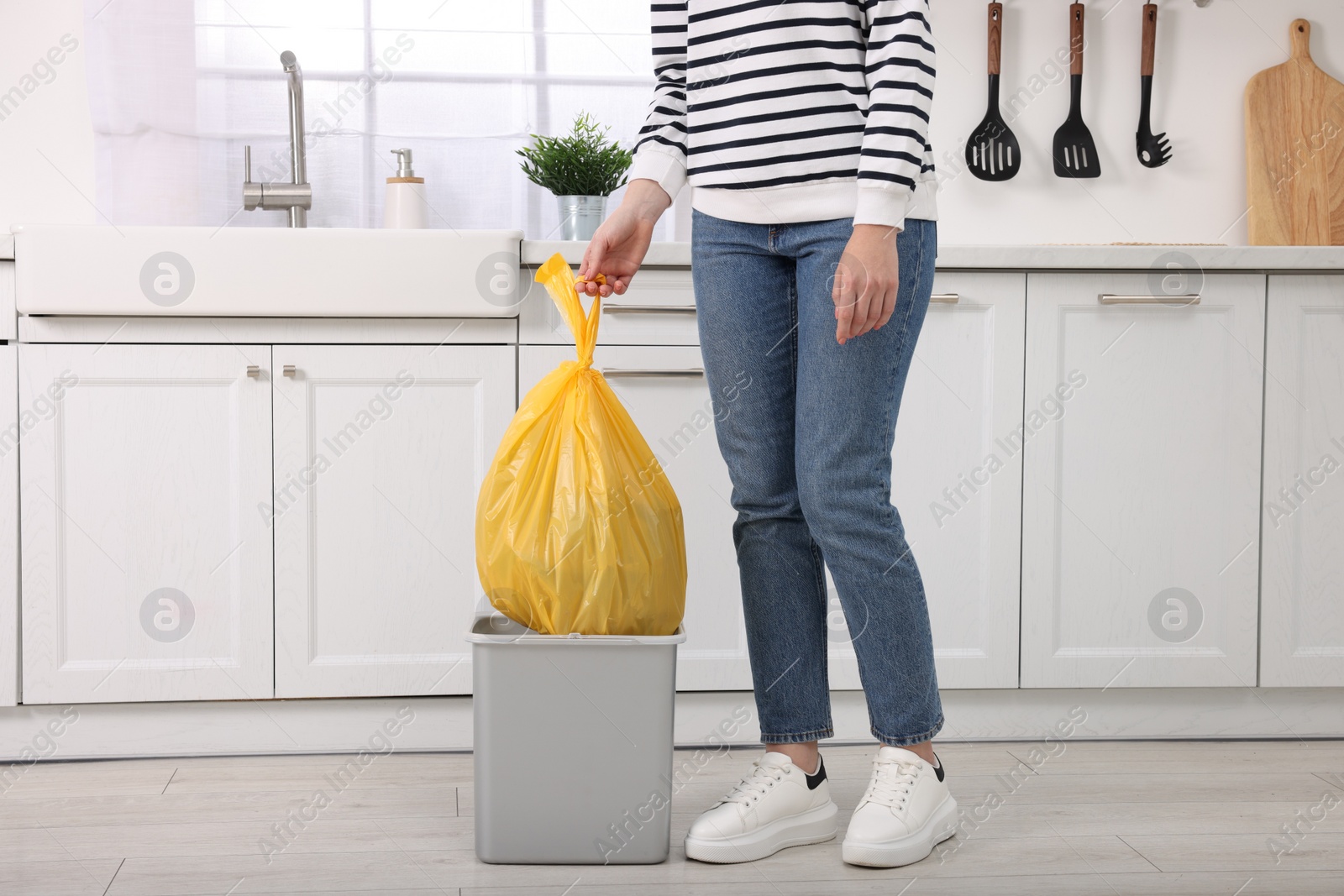 Photo of Woman taking garbage bag out of trash bin in kitchen, closeup