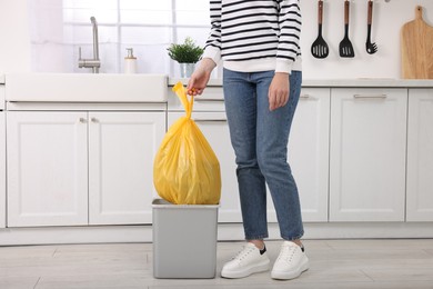 Photo of Woman taking garbage bag out of trash bin in kitchen, closeup