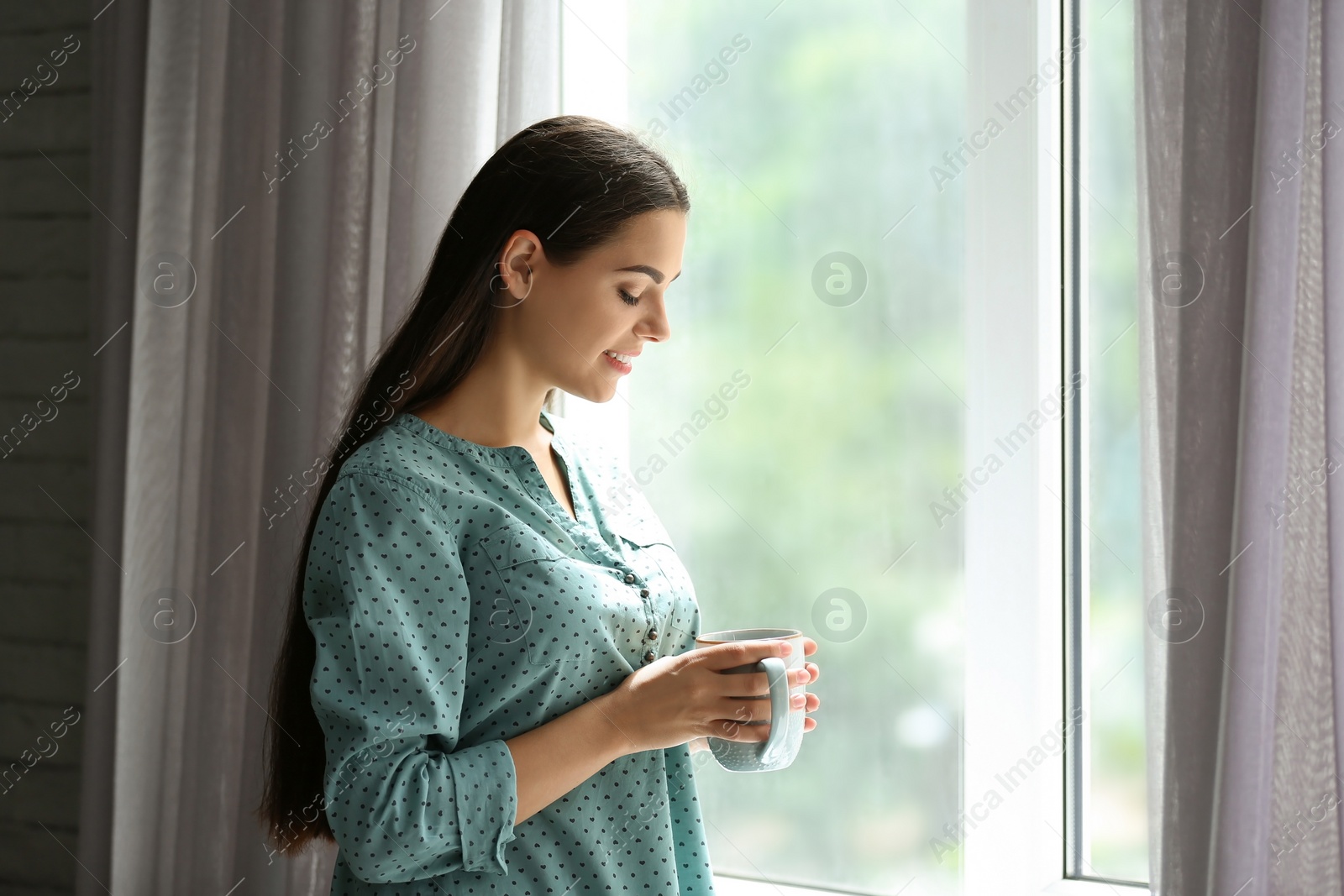 Photo of Young beautiful woman drinking morning coffee near window at home