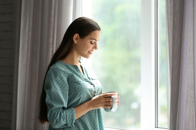 Young beautiful woman drinking morning coffee near window at home