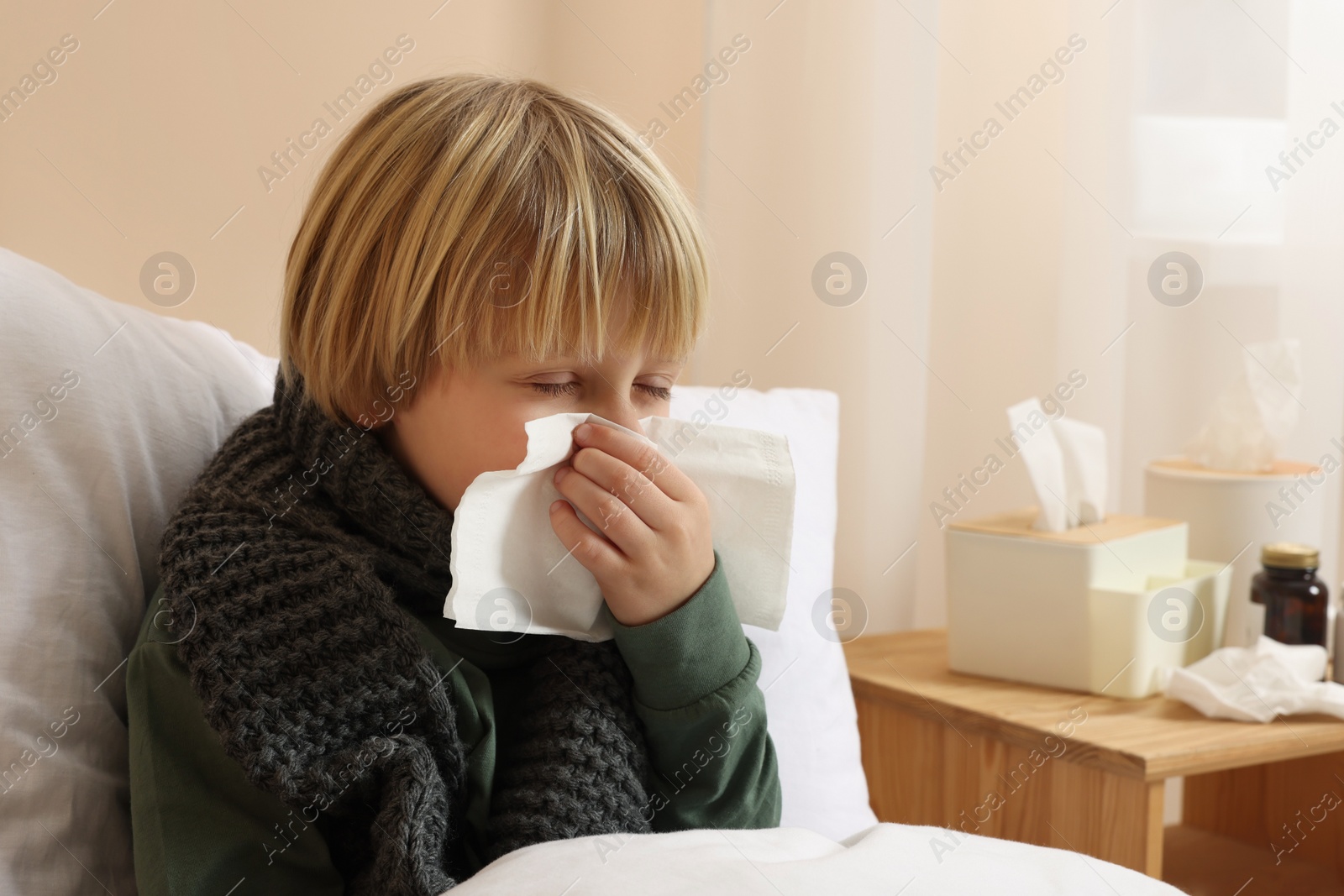 Photo of Boy blowing nose in tissue in bed at home. Cold symptoms