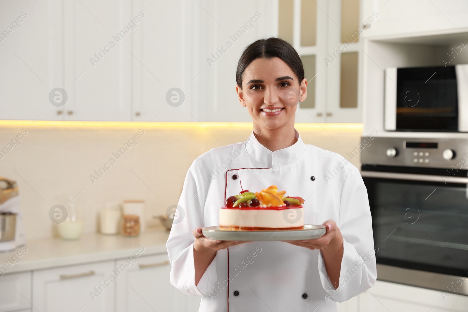 Photo of Happy professional confectioner holding delicious cake in kitchen