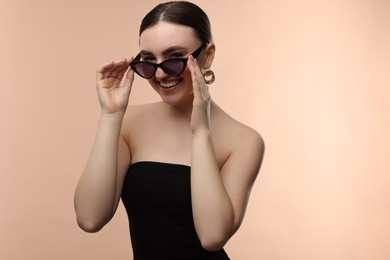 Portrait of beautiful young woman with sunglasses on beige background