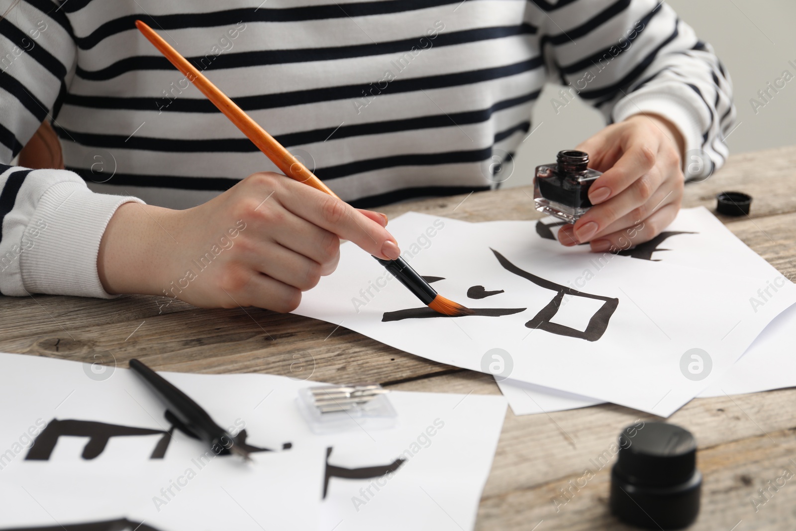 Photo of Calligraphy. Woman with brush and inkwell writing hieroglyphs on paper at wooden table, closeup