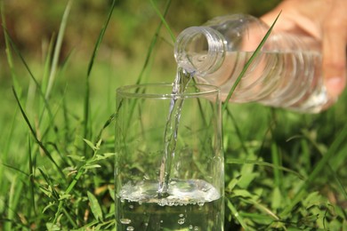 Woman pouring pure water into glass outdoors on sunny day, closeup