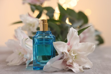 Bottle of perfume and beautiful lily flowers on table against beige background with blurred lights, closeup