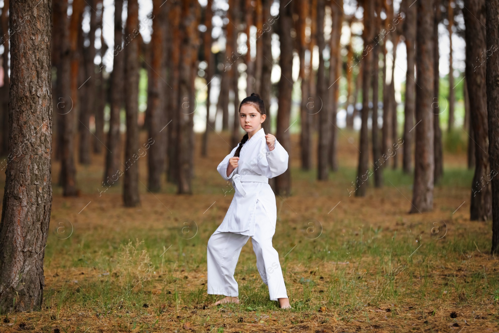 Photo of Cute little girl in kimono practicing karate in forest