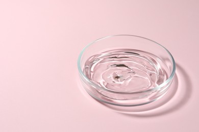 Photo of Petri dish with liquid on pale pink background, space for text