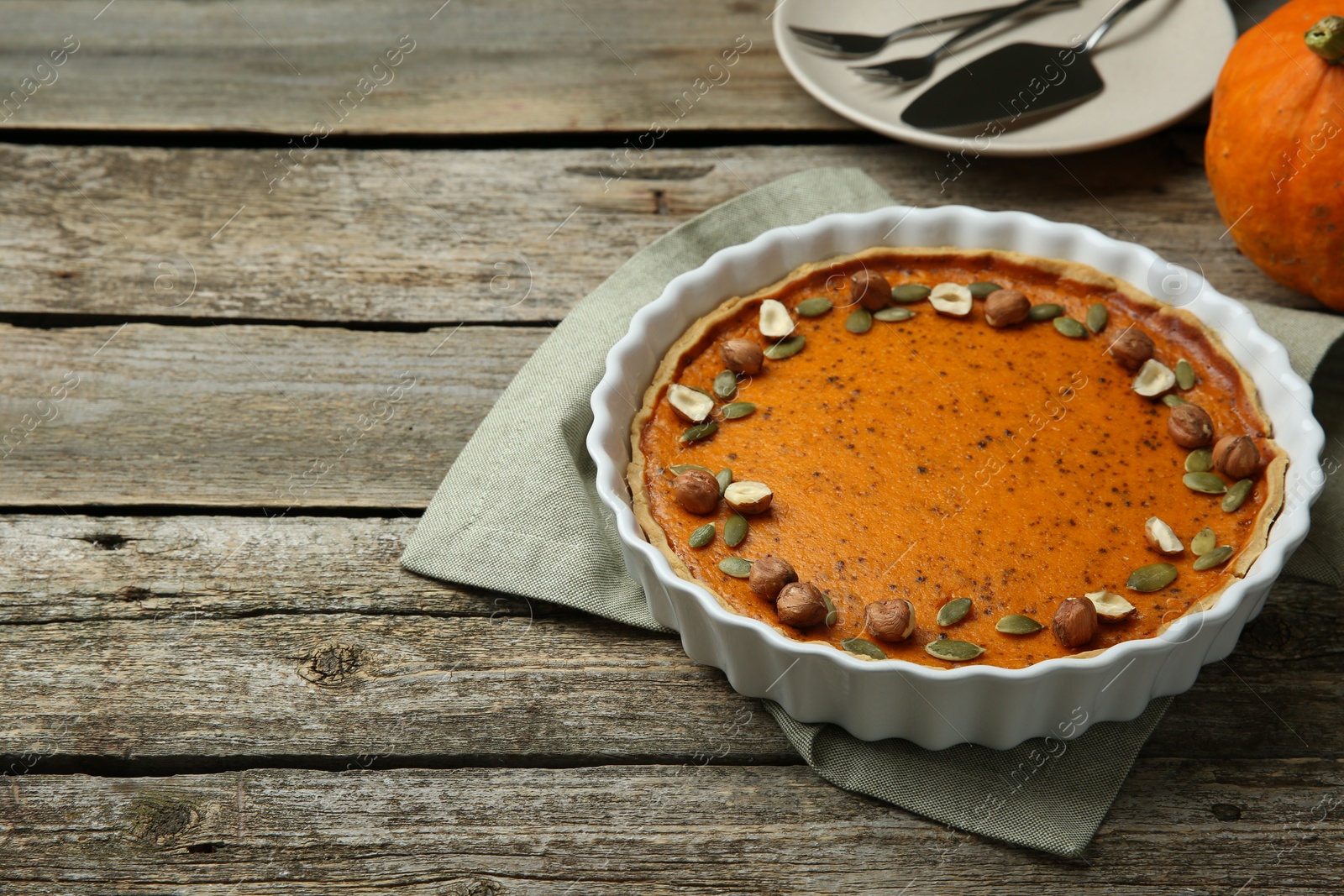 Photo of Delicious pumpkin pie with seeds and hazelnuts on wooden table. Space for text