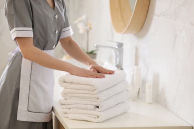 Young chambermaid with stack of fresh towels in bathroom, closeup