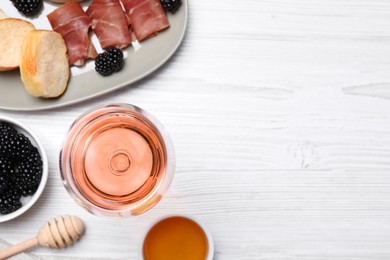 Glass of delicious rose wine and snacks on white wooden table, flat lay. Space for text
