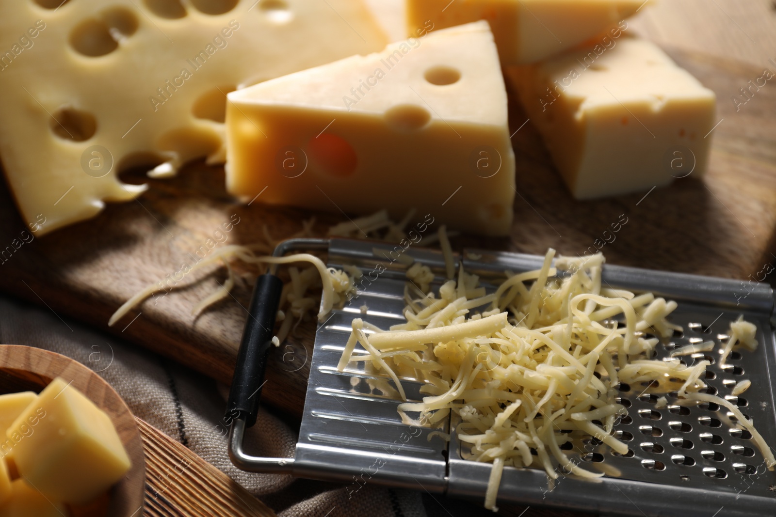 Photo of Grated, cut cheese and grater on table, closeup