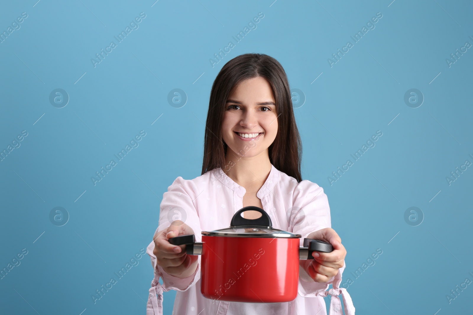 Photo of Happy young woman with cooking pot on light blue background