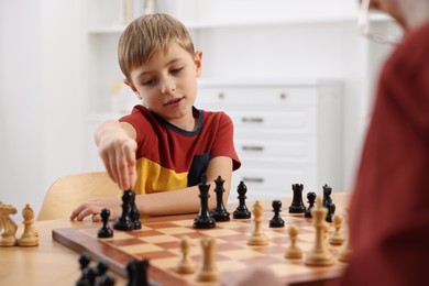 Photo of Little boy playing chess with his grandfather at table in room