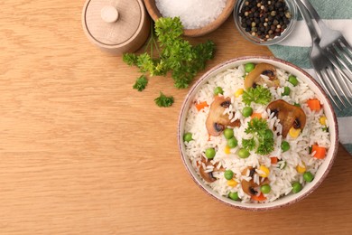 Photo of Bowl of delicious rice with vegetables on wooden table, flat lay. Space for text