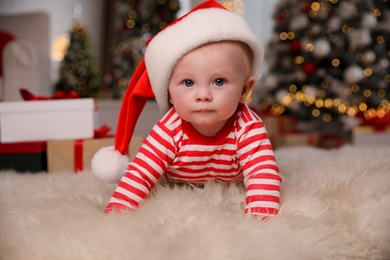 Photo of Cute little baby in bright pajamas and Santa hat on floor at home. Christmas suit