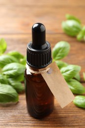 Photo of Glass bottle of basil essential oil and leaves on wooden table, closeup