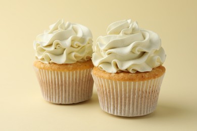 Tasty vanilla cupcakes with cream on pale yellow background