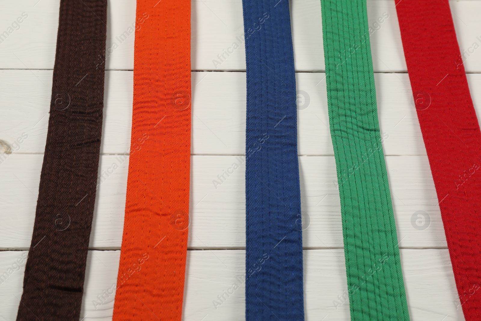 Photo of Colorful karate belts on wooden background, flat lay